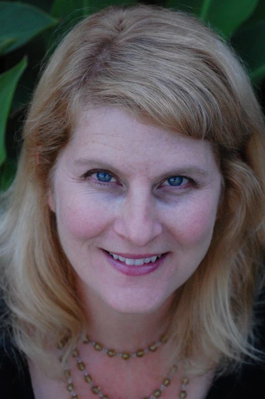 a woman wearing a necklace next to a bush