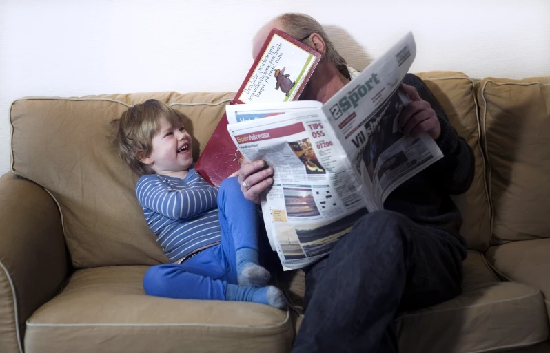 an adult reading a magazine with his son