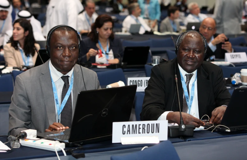 two men in business attire sitting at a table with laptops