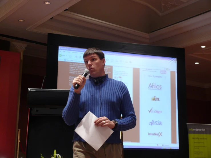 a man in blue sweater speaking into microphone at event