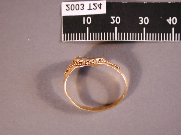 a gold ring with filigrees is beside a ruler