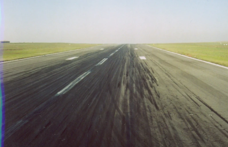 an empty runway with yellow grass and an open field in the background