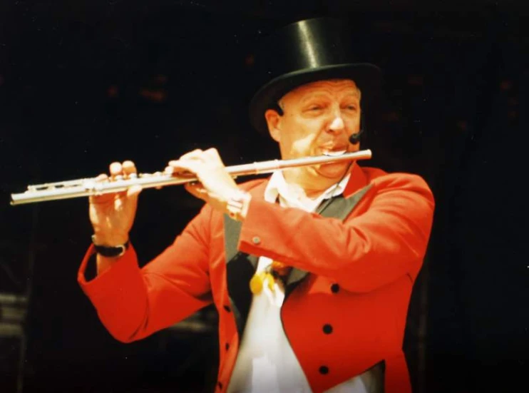 a man in a red suit with a black top hat playing a flute