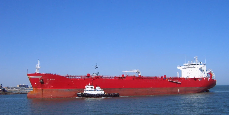 a large red ship in the water by a dock