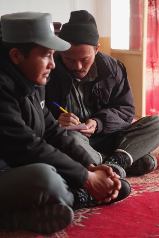 two asian guys sitting on the floor looking at a note