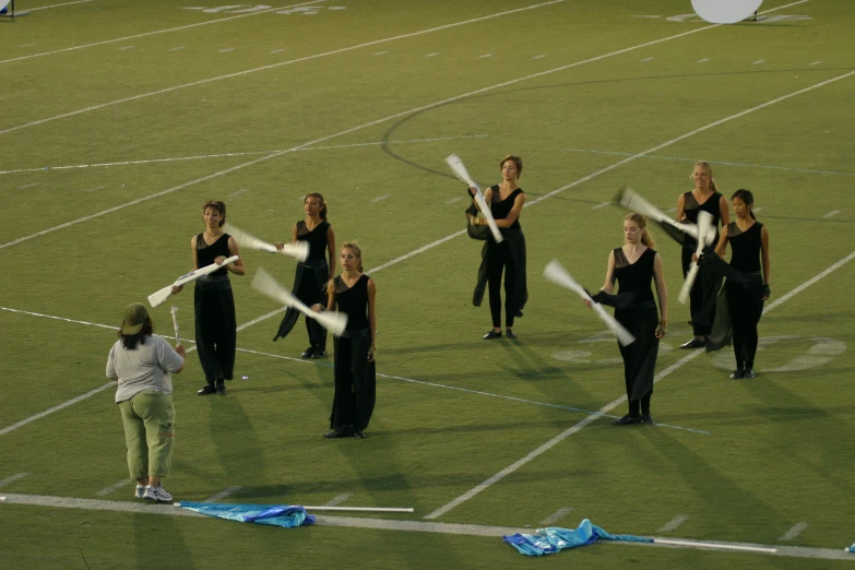 some female marching team members holding sticks on a field