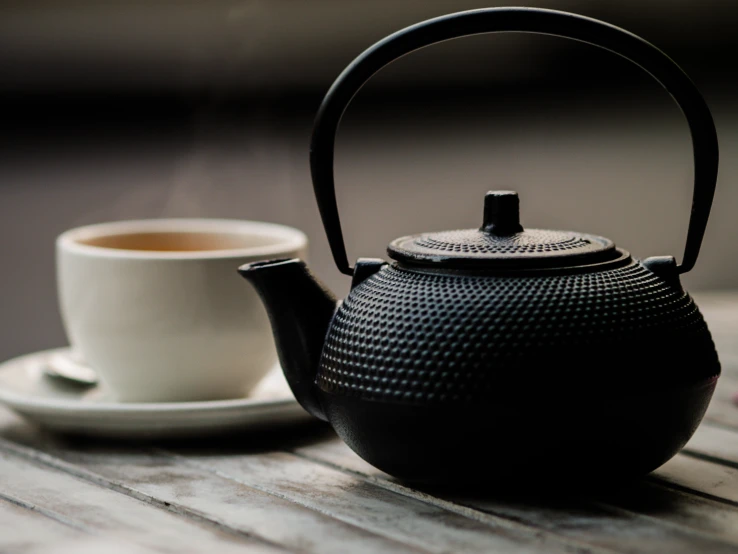 a black teapot with a mug on a table