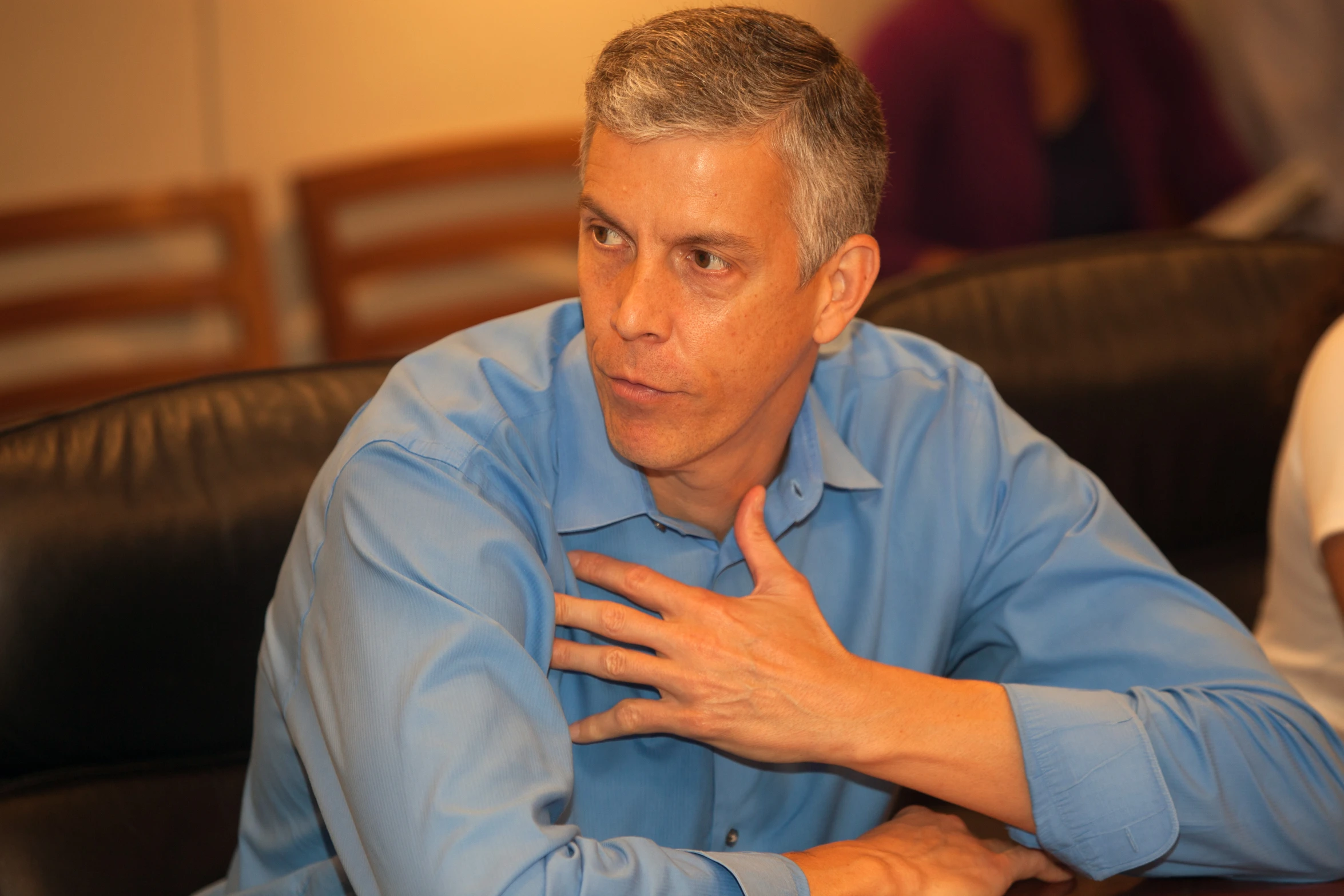 a man in a blue shirt at a conference with hands on his chest