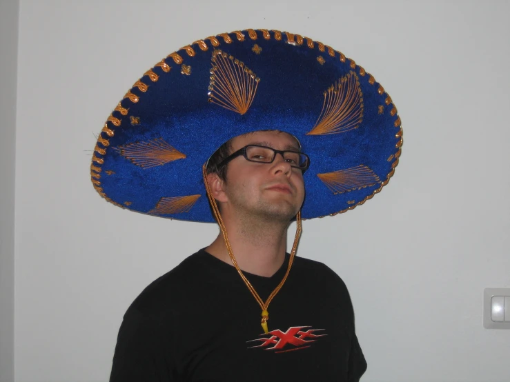 a man wearing a large blue sombrero while standing in the corner
