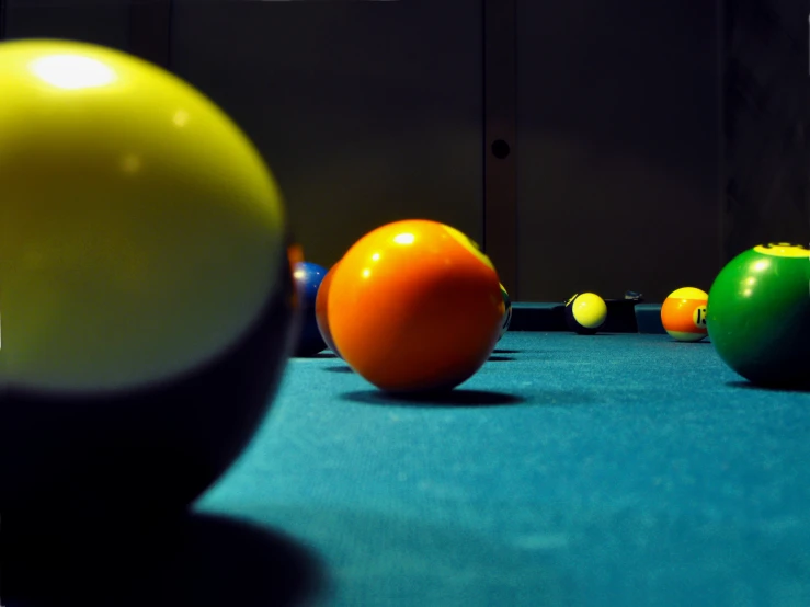 billiards balls, a pool stick, and an orange on a pool table