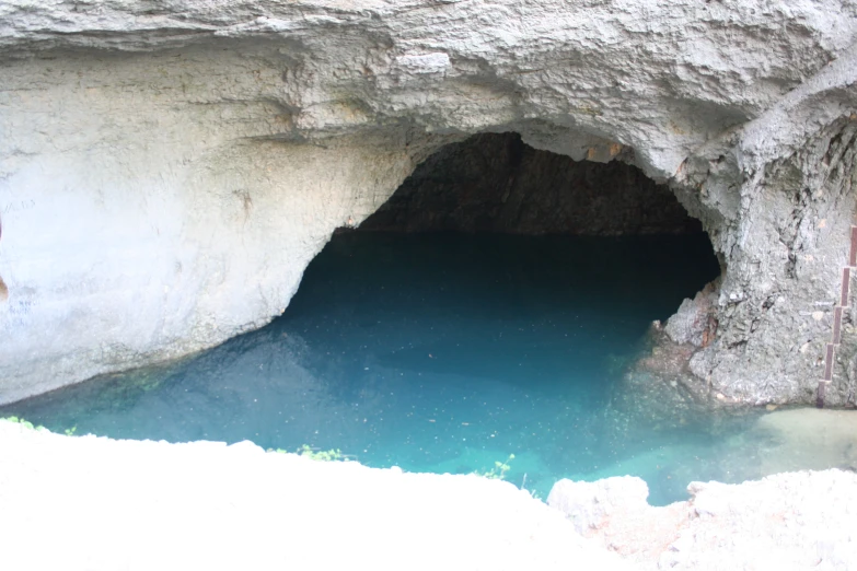 an open blue - water cave in the mountains near some water