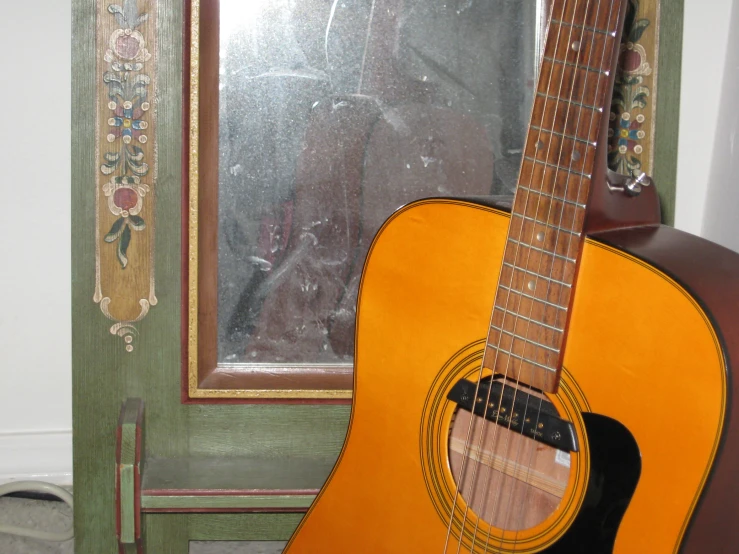 an old acoustic guitar sitting next to a mirror