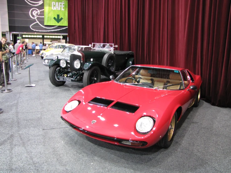 two vintage cars are parked in front of a red curtain