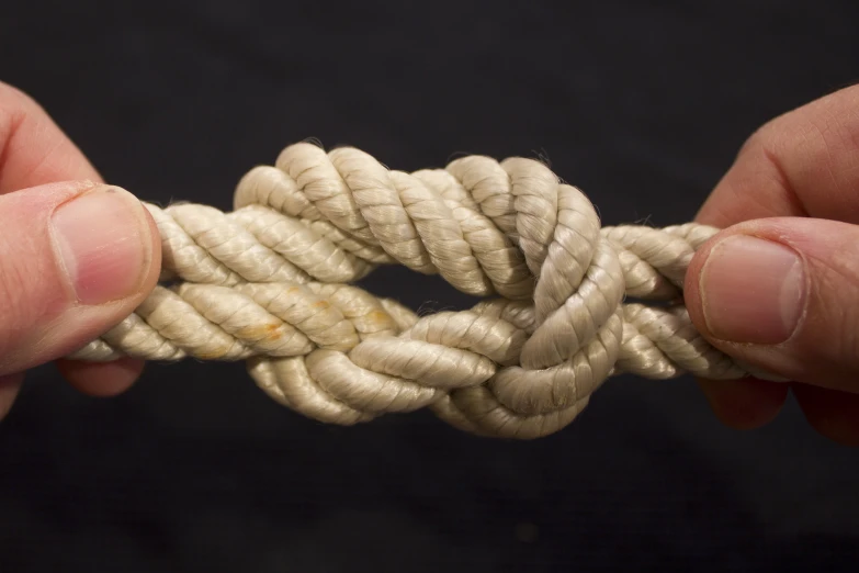 hands holding up a piece of rope that has been knotted together