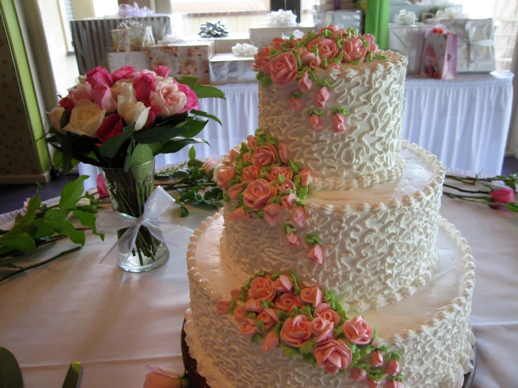 a 3 - tier white wedding cake sitting on a table next to flowers