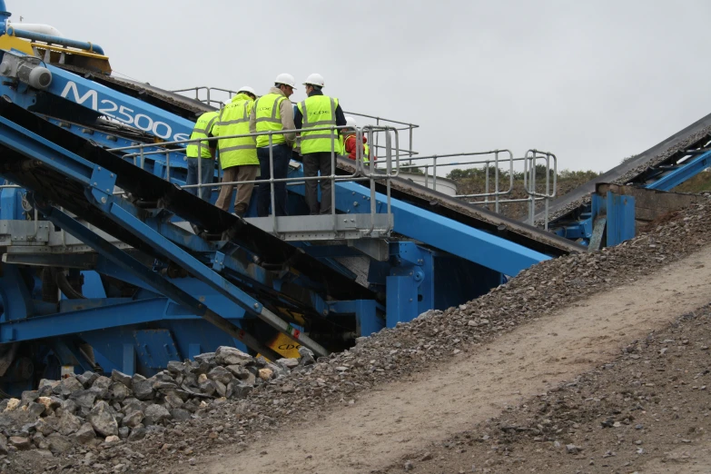 workers standing near large pile of rubble under cloudy sky