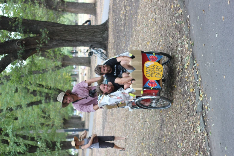 three people ride on a bicycle with a cardboard box