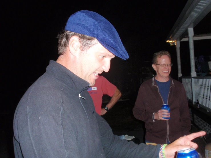 two guys laughing together while one holding a bottle of beer