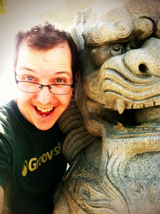 man taking po of himself in front of stone lion sculpture