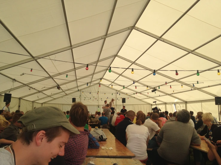 several people sit around tables with food in a tent