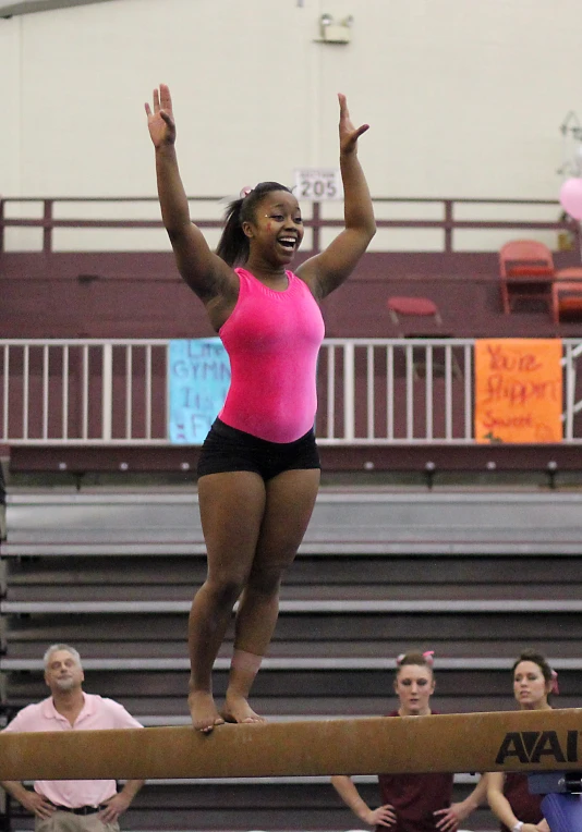 woman in a pink shirt and black shorts doing on beam in gym