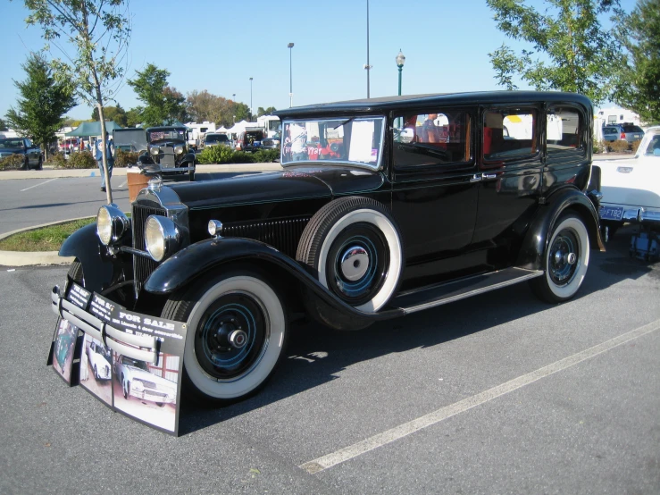 an old black car parked in a parking lot next to another white car