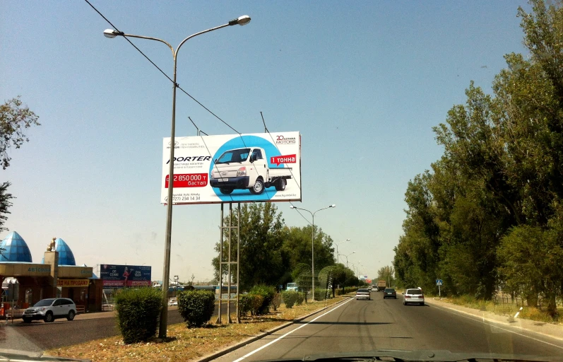 a city street with lots of traffic passing by an advertising billboard on a lamppost