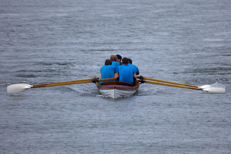 four rowers in blue shirts row down the river