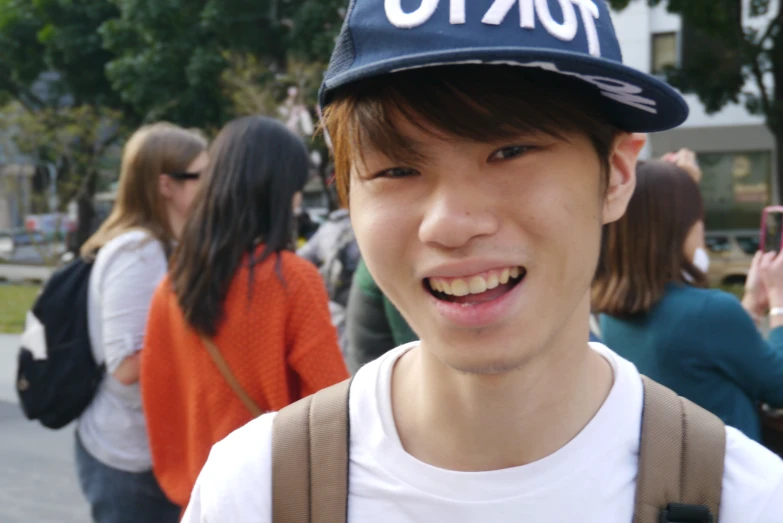 a young asian man wearing a tokyo hat in front of several people