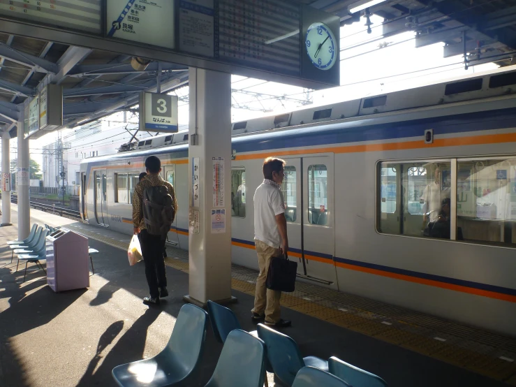 two people standing on a train platform waiting for the train to arrive