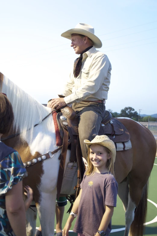 a little girl smiles as she rides a horse with a man in the back