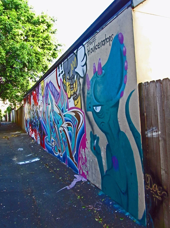 graffiti on a side of a wall with a wooden fence and trees