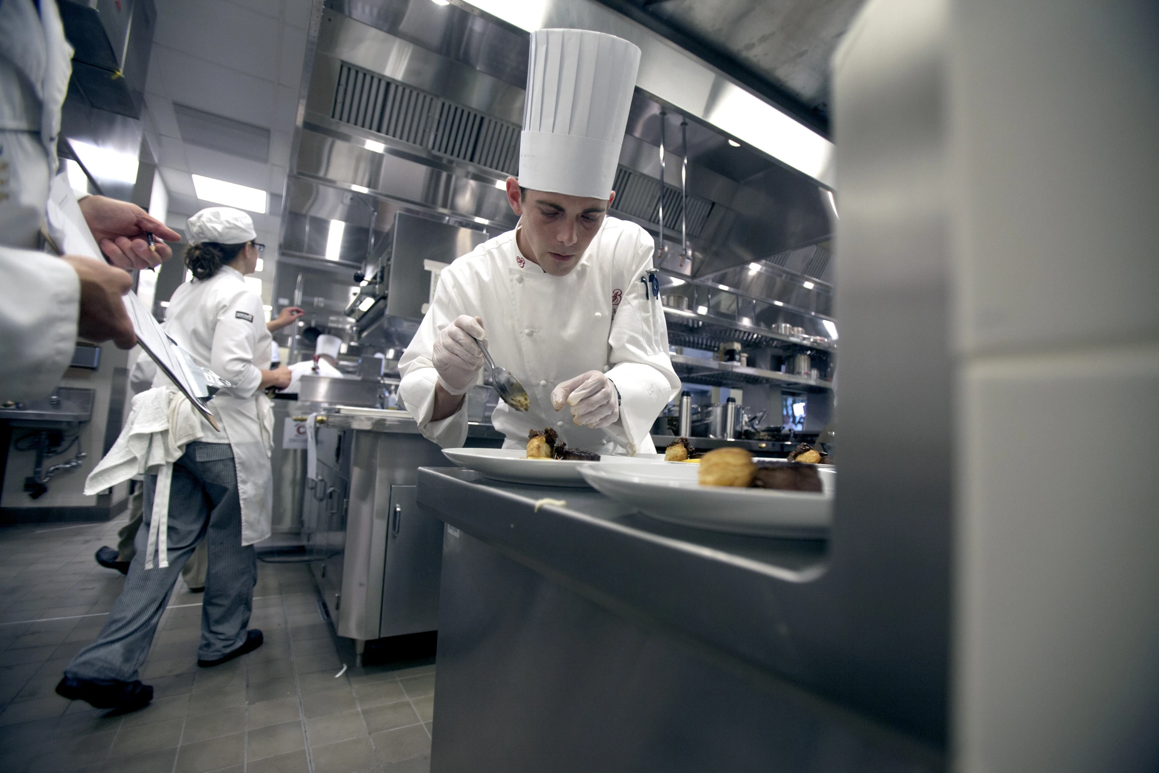 chefs making desserts and doing food on trays in large kitchen