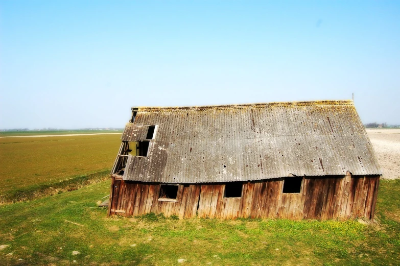 an old rundown barn in the middle of a large open field