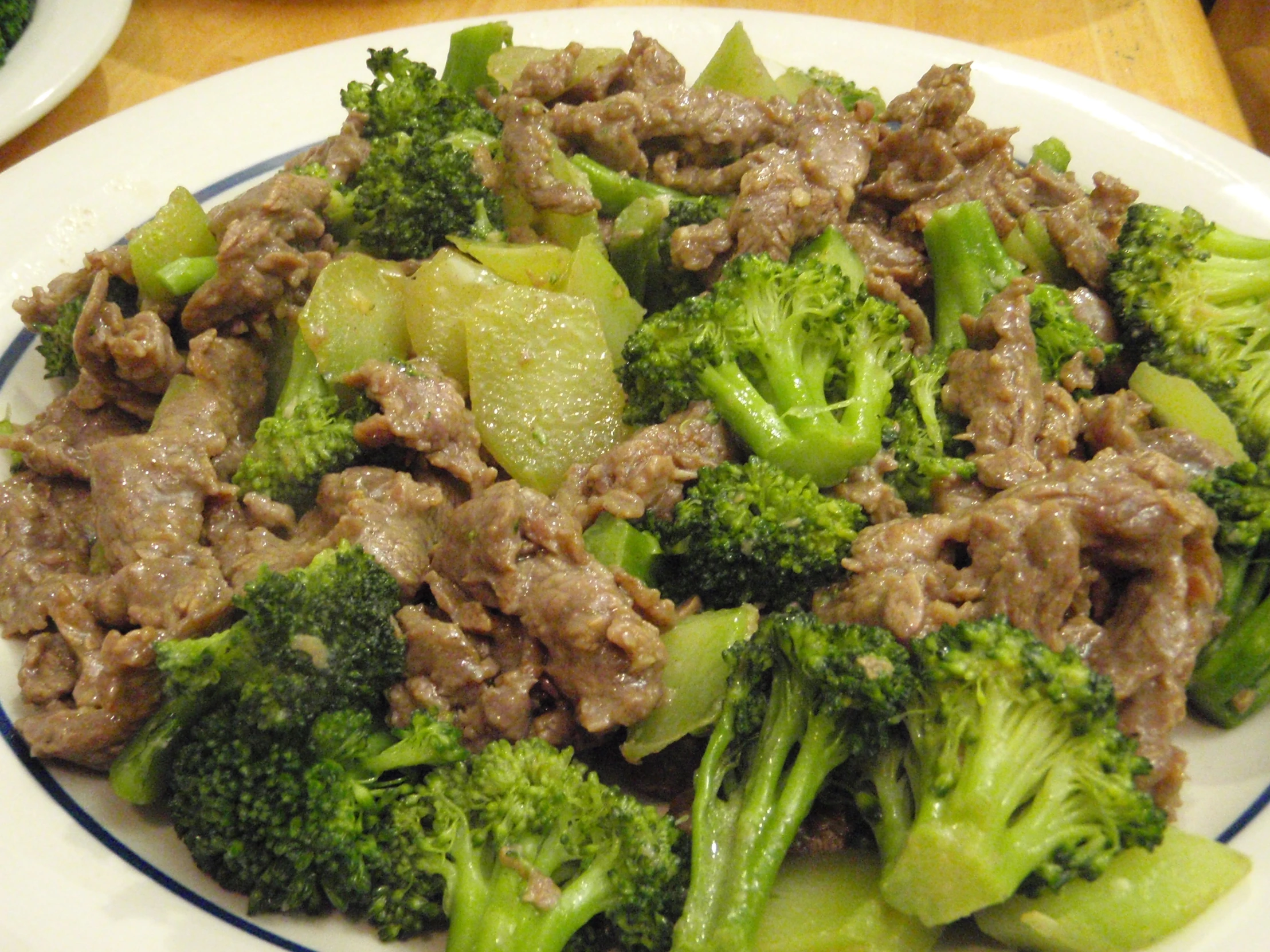 beef and broccoli on a white plate with a blue border