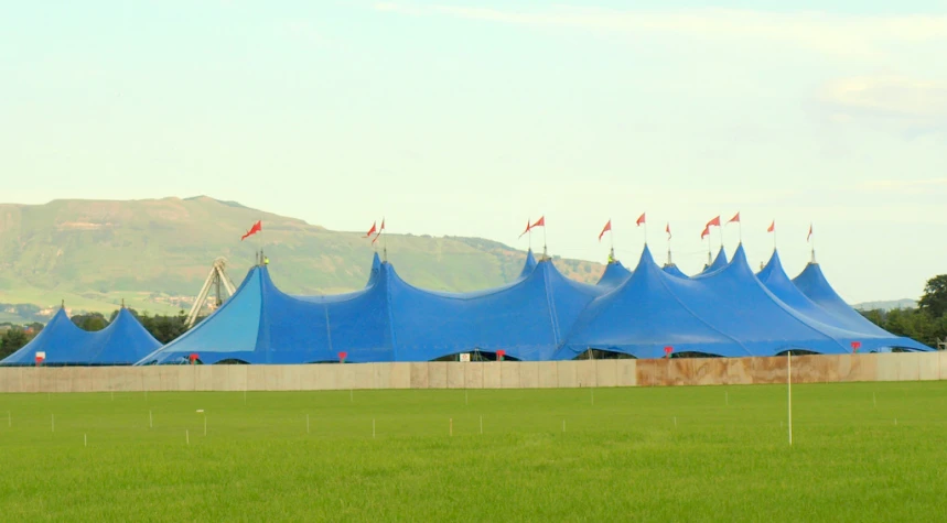 blue tents lined up in the grass beside a fence