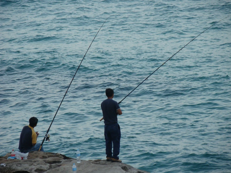 man fishing with two rod on rock next to ocean