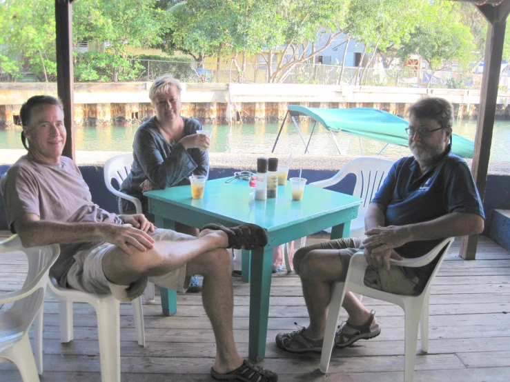 three people sit at a table near the water