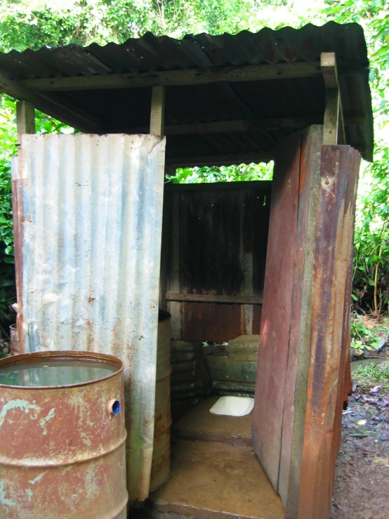 a rusted steel outhouse with two trash containers