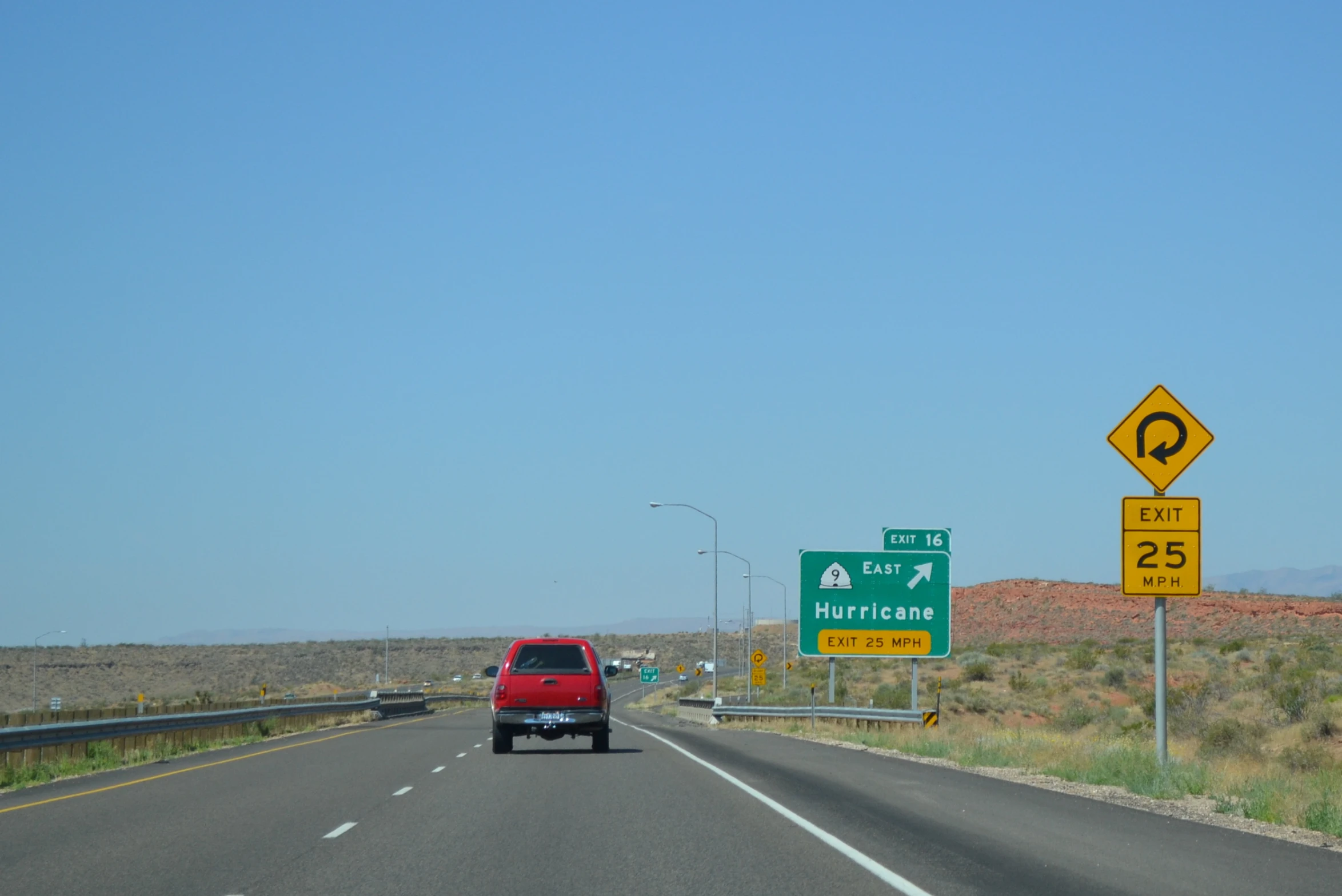 a red car driving on a highway near a green sign