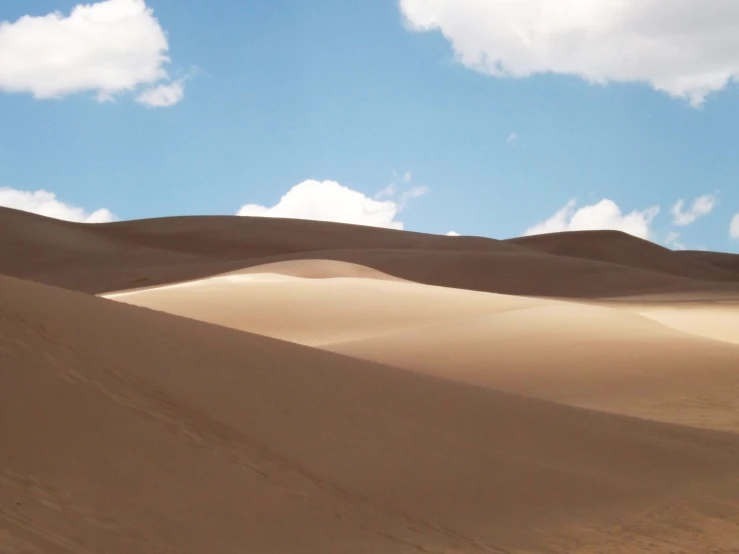 a large sand dune sitting below a blue sky with fluffy white clouds