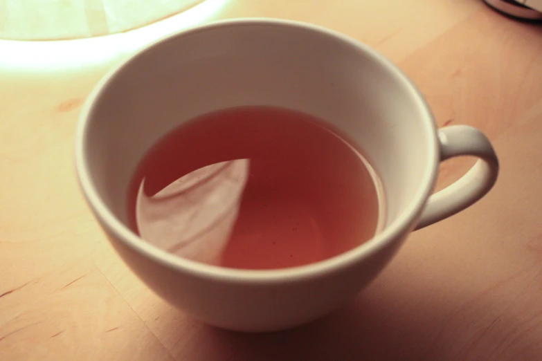 a small white mug is filled with tea and a piece of paper
