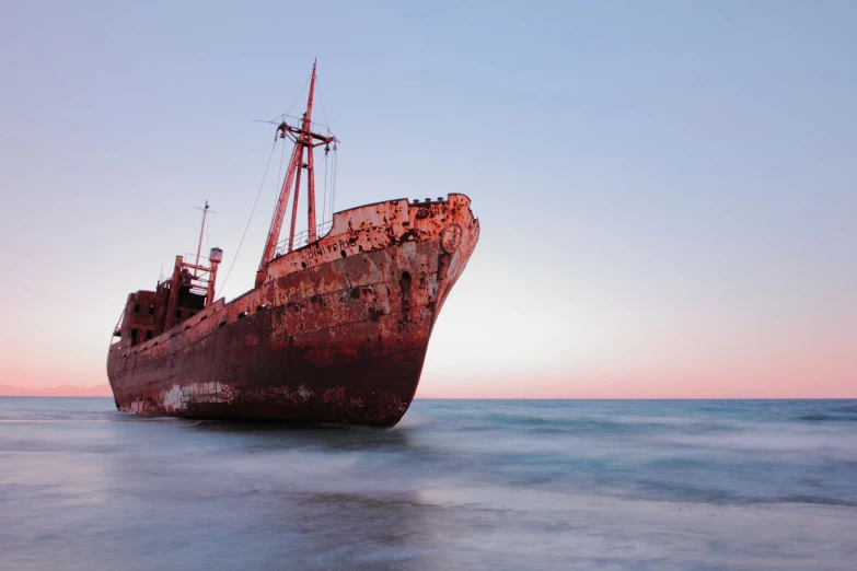 a red ship in the ocean during sunset