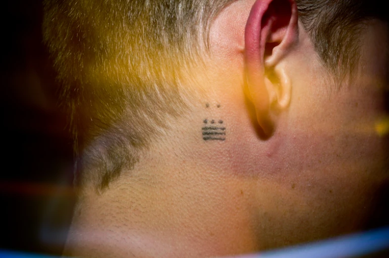 a guy with ear piercing and a piece of lettering tattoo on his side of neck