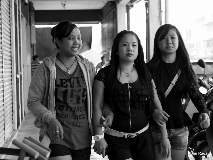 three women are walking down a sidewalk, two of them are smiling