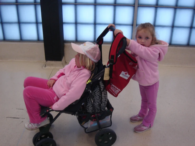 two girls in pink jackets are pulling soing in a stroller