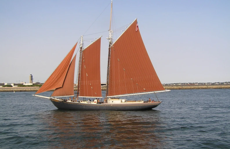 an old sailboat with red sails is sailing in the water
