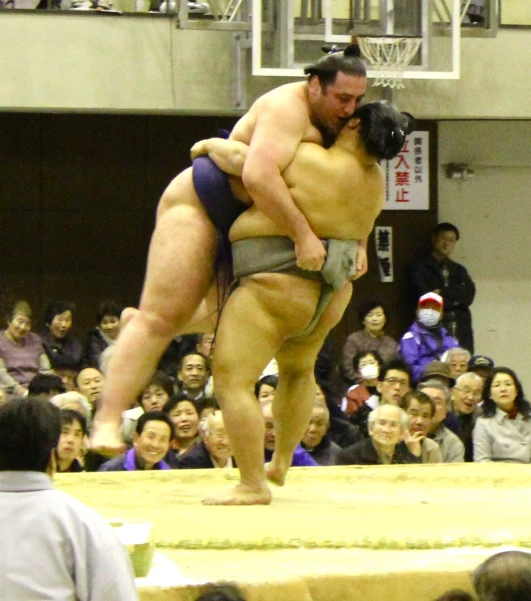 an sumo wrestler in a blue outfit wrestling a competitor