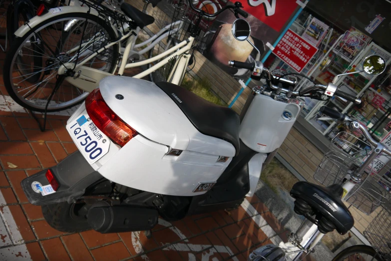 a white scooter is sitting on the ground next to some bikes