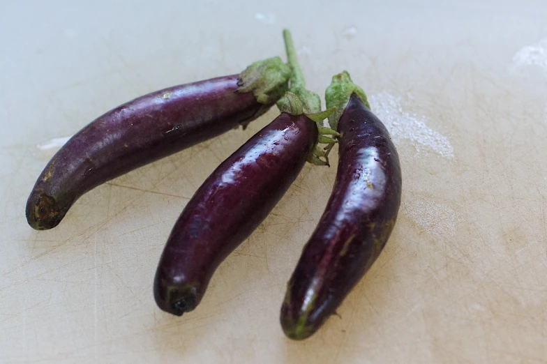 three small purple eggplants sitting on a white surface